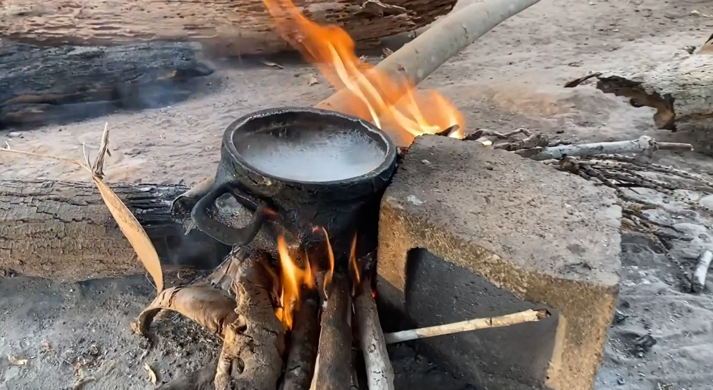 The image shows a pan with boiling water over a communal fire. 
